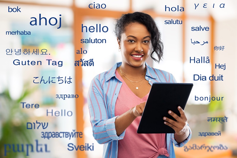 Happy woman using tablet computer over greeting words in different foreign languages for article on niche language translations in the U.S.